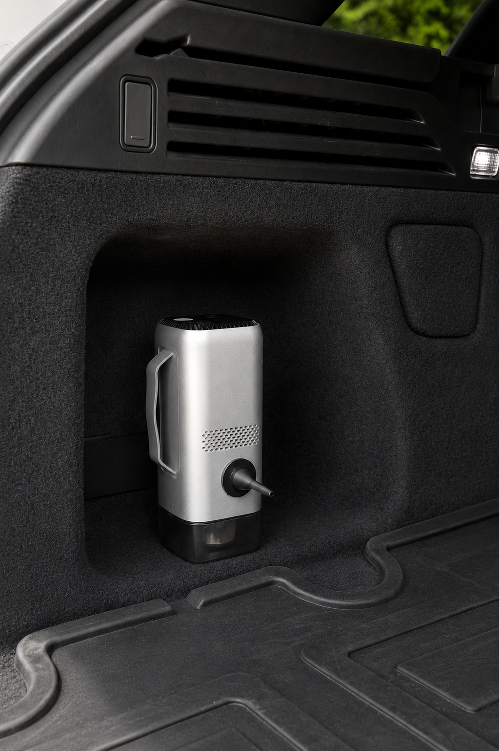 A silver and black portable car emergency device with a handle, shown sitting in a black compartment of a vehicle boot